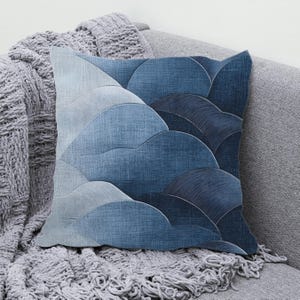May include: A blue and white decorative pillow with a geometric pattern of overlapping waves. The pillow is made of a soft, textured fabric and has a subtle sheen.