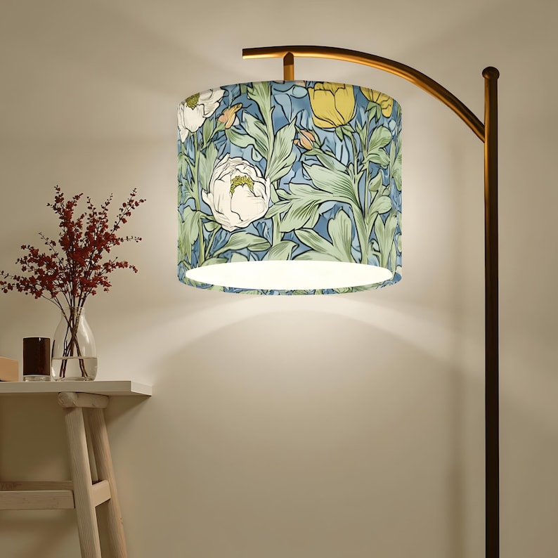 May include: A floor lamp with a floral patterned lampshade. The lampshade features a design of white and yellow flowers with green leaves on a blue background. The lamp has a curved, bronze-colored metal frame.