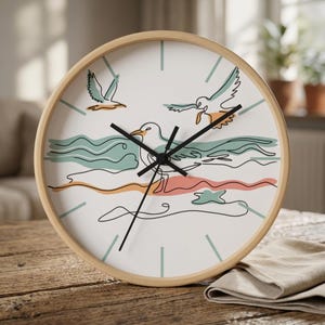 May include: A round wall clock with a light wood frame and a white face featuring a continuous line drawing of seagulls and ocean waves in muted teal, orange, and black. The clock has black hour, minute, and second hands and teal tick marks.