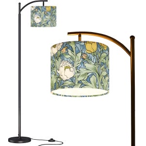 May include: A black arc floor lamp with a floral patterned lampshade. The lampshade features a design of white peonies, yellow flowers, and green leaves on a blue background. The lamp has a round base and a curved arm.