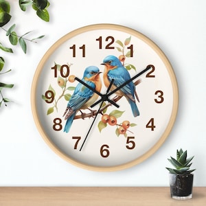 May include: A white clock with a wooden frame features a bluebird design with brown branches and berries. The clock face has black Roman numerals and black hands.