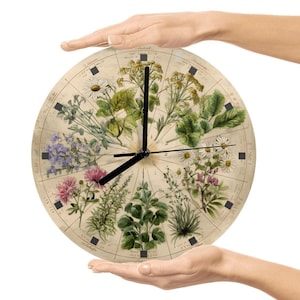 May include: A round clock featuring botanical illustrations of various flowers and plants. The clock face has a vintage, aged appearance with black hands and hour markers. The clock is held by two hands against a white background.