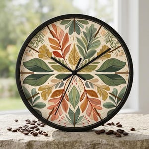 May include: A round wall clock with a black frame and a cream-colored face featuring a symmetrical botanical pattern of leaves in shades of sage green, mustard yellow, and terracotta orange. The clock has thin black hands and no numerals.