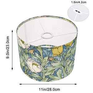 May include: Cylindrical lampshade with a floral pattern. The shade is 9.0 inches (23.0 cm) tall and 11 inches (28.0 cm) in diameter. The design features white and yellow flowers with green leaves on a blue background. The top opening is 1.6 inches (4.2 cm) in diameter.