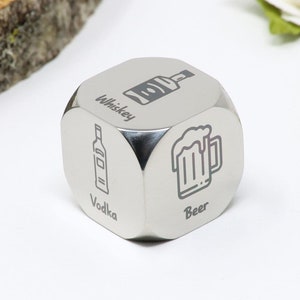 May include: A silver metal dice with six sides, each side has a different drink icon and name. The sides show a beer mug with the word "Beer", a bottle with the word "Vodka", a bottle with the word "Whiskey", a bottle with the word "Gin", a bottle with the word "Rum", and a bottle with the word "Tequila".