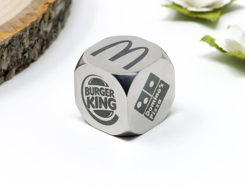 Pode incluir: Um dado de metal prateado com os logotipos do McDonald's, Burger King e Domino's Pizza.