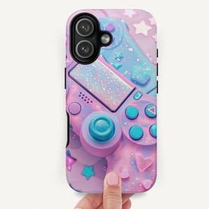 May include: A phone case featuring a pastel pink and blue video game controller design. The case has a glittery finish and is decorated with stars and hearts. The camera lenses are visible at the top.