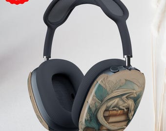 May include: Dark gray over-ear headphones with a fantasy-themed design. The earcups feature a detailed illustration of a white dragon resting on a stack of books, with a backdrop of mountains and clouds. The headphones have a padded headband.