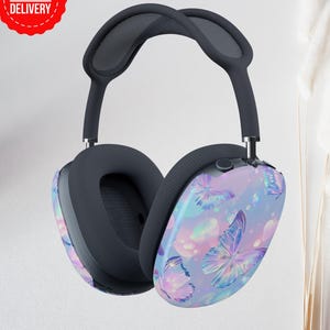 May include: Wireless over-ear headphones with a butterfly design. The earcups feature a pastel purple, blue, and pink butterfly pattern. The headband and earcups are dark gray. The headphones have a mesh top and a Fast Delivery sticker.