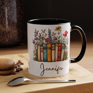 Personalized ceramic mug with black handle featuring a row of colorful books with blooming wildflowers and a custom name “Jennifer” in script – spiritual gift for readers and teachers.