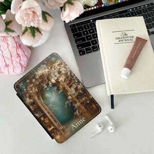 Kindle Paperwhite folio case with vintage bookshelf arch artwork styled on a cozy knit blanket next to a candle and coffee.
