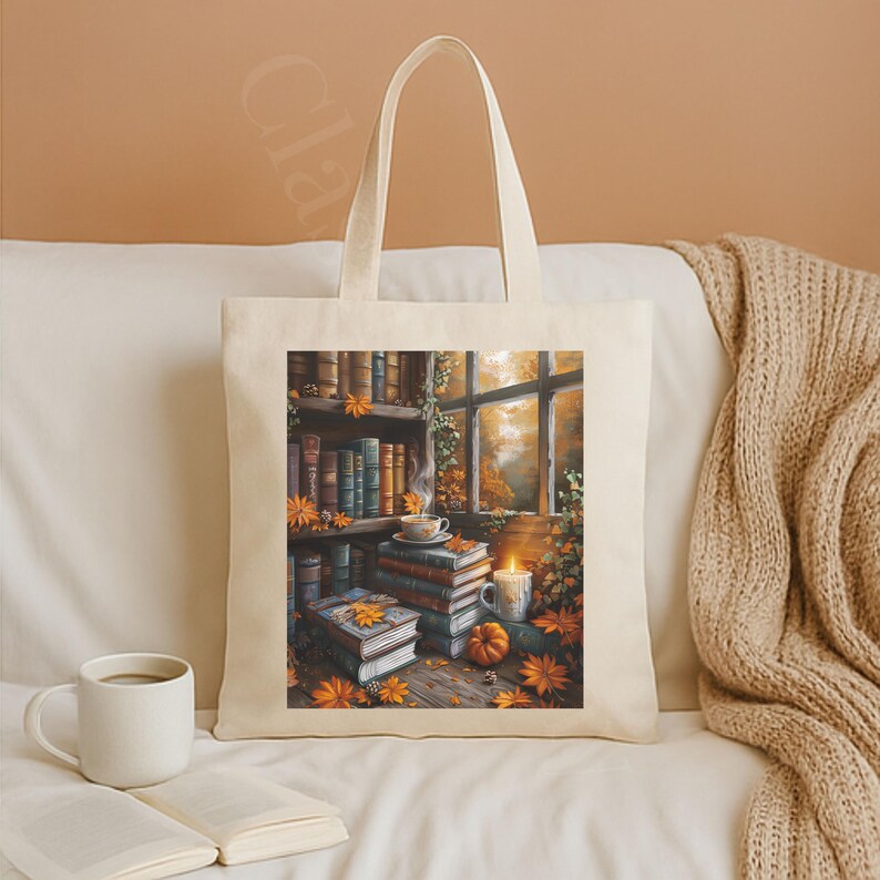 Cotton canvas tote bag featuring a cozy autumn library scene with stacked vintage books, a steaming coffee cup, glowing candle, pumpkins, and fall leaves by the window. Perfect gift for book lovers and cozy fall style