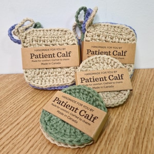 May include: A selection of handmade crochet items in beige, green, and blue. The image shows two square washcloths with loops and two round coasters. Each item has a brown tag with the text "Patient Calf".