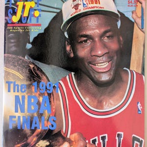May include: A magazine cover featuring a smiling man wearing a Chicago Bulls jersey and a white hat that says "World Champions 1991." The magazine title is "Jr. Stuff" with the text "The Sports Collecting Magazine for Kids." The cover also reads "The 1991 NBA Finals."