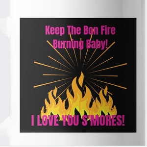 Może przedstawiać: Biały ceramiczny kubek z czarnym kwadratem z ilustracją ogniska. Tekst brzmi "Keep The Bon Fire Burning Baby! I Love You S'Mores!" w kolorze różowym i żółtym. Kubek ma biały uchwyt.