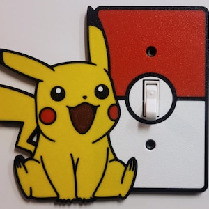 May include: A yellow Pikachu-themed light switch cover with a matching Pikachu cutout. The switch plate is red and white, resembling a Poké Ball. The design features a white toggle switch and black outlines.