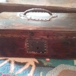 May include: A dark brown wooden box with a leather handle and metal accents. The box has a metal latch and is secured with metal studs.