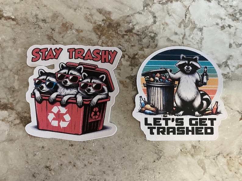 Puede incluir: Dos pegatinas con mapaches. Una muestra tres mapaches en un cubo rojo con el texto "STAY TRASHY". La otra muestra un mapache con un cubo de basura y una cerveza, con el texto "LET'S GET TRASHED".