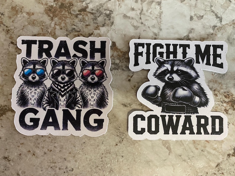 Puede incluir: Dos pegatinas con ilustraciones de mapaches. Una dice "Trash Gang" con tres mapaches con gafas de sol. La otra dice "Fight Me Coward" con un mapache con guantes de boxeo.
