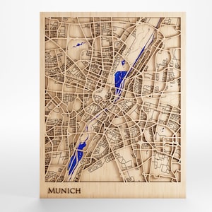 Pode incluir: Um mapa de madeira de Munique, Alemanha, com as ruas da cidade e o rio esculpidos. O mapa é pintado de azul e está montado em uma moldura de madeira. A palavra "MUNICH" está impressa abaixo do mapa.