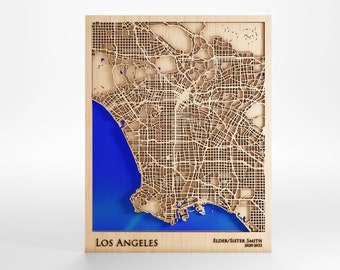 May include: A wooden map of Los Angeles with a blue background. The map is laser cut and shows the city streets. The text "LOS ANGELES" is printed below the map, and the text "ELDER/SISTER SMITH 2020-2023" is printed below the text "LOS ANGELES".