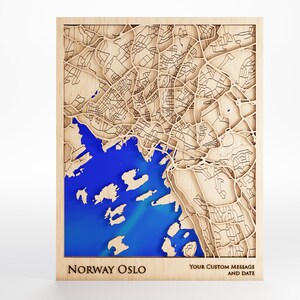 May include: Wooden map art of Oslo, Norway with a blue resin inlay. The map is framed and has the text "Norway Oslo" and "Your Custom Message and Date" at the bottom.
