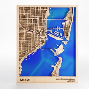 May include: A wooden map of Miami, Florida, with a blue water feature. The map is framed and has the word "MIAMI" printed at the bottom left corner. The bottom right corner has the text "YOUR CUSTOM MESSAGE AND DATE".