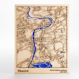 May include: A wooden map of Prague with a blue river carved into the wood. The map is framed and has the word "PRAGUE" printed below it. The text "YOUR CUSTOM MESSAGE AND DATE" is printed below the map.