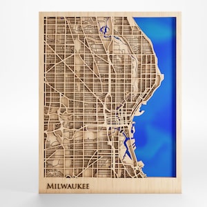 May include: A wooden map of Milwaukee, Wisconsin, with a blue lake cutout. The map is framed in wood and has the city name "MILWAUKEE" printed below the map.