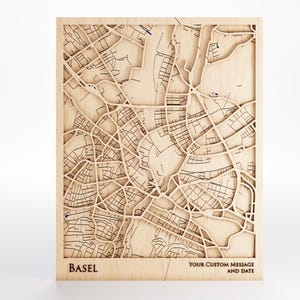 Peut inclure: Une carte en bois de Bâle, Suisse, avec des détails complexes des rues et des bâtiments. Le nom de la ville est en bas à gauche, avec un espace pour un message personnalisé et une date. La carte est en bois clair.