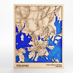 May include: A wooden map of Helsinki, Finland, with a blue water feature. The map is framed and has the word "Helsinki" printed below it. The text "Your Custom Message and Date" is printed below the map.