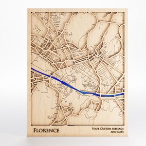 May include: A wooden map of Florence, Italy, with a blue river running through it. The map is intricately carved, showing streets and buildings. The word "FLORENCE" is at the bottom, with space for a custom message and date.