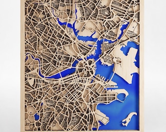 May include: A rectangular wooden wall map of Boston featuring intricate laser-cut street patterns in light wood tones layered over a vibrant blue water base. The text BOSTON is at the bottom left, and THE JOHNSON FAMILY OUR FIRST HOME 2026 is at the bottom right.
