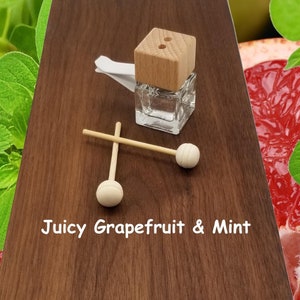 May include: A small glass bottle with a wooden lid and two wooden sticks with round ends. The bottle is filled with a clear liquid. The text "Juicy Grapefruit & Mint" is printed on a wooden surface.