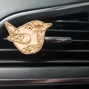 Può includere: Un profumatore per auto in legno a forma di uccello con dettagli intricati. L'uccello è di colore marrone chiaro e presenta un design dettagliato.