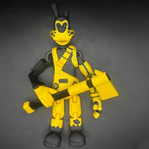 Könnte beinhalten: Eine gelb-schwarze, bewegliche Actionfigur einer Zeichentrickfigur, die eine gelb-schwarze Axt hält. Die Figur hat ein gelbes Gesicht, Latzhosen und Hände, mit schwarzen Armen, Beinen und Füßen. Die Figur ist vor einem schwarzen Hintergrund posiert.