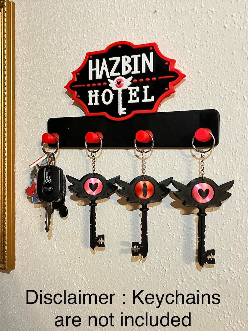 May include: Black key-shaped wall hook with red accents. The hook has four key rings and a sign that reads "Hazbin Hotel" in red and white letters. Disclaimer: Keychains are not included.