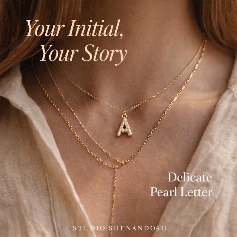 Pu&ograve; includere: Collane dorate a strati con un ciondolo iniziale tempestato di perle. La lettera "A" &egrave; il punto focale, con il testo "Your Initial, Your Story" e "Delicate Pearl Letter". Il logo Studio Shenandoah &egrave; in basso.