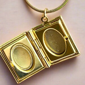 May include: A gold-toned locket necklace with a book-shaped pendant. The locket opens to reveal two oval-shaped compartments.