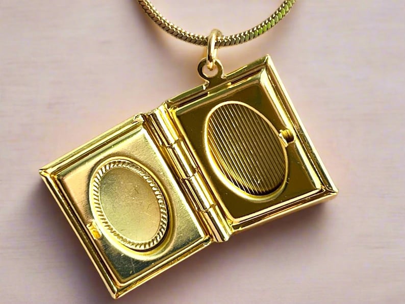 May include: A gold-toned locket necklace with a book-shaped pendant. The locket opens to reveal two oval-shaped compartments.