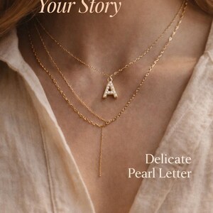Pu&ograve; includere: Collana a strati color oro con un ciondolo a forma di lettera "A" tempestato di perle. L'immagine include il testo "Your Initial, Your Story" e "Delicate Pearl Letter". Il logo Studio Shenandoah &egrave; in basso.