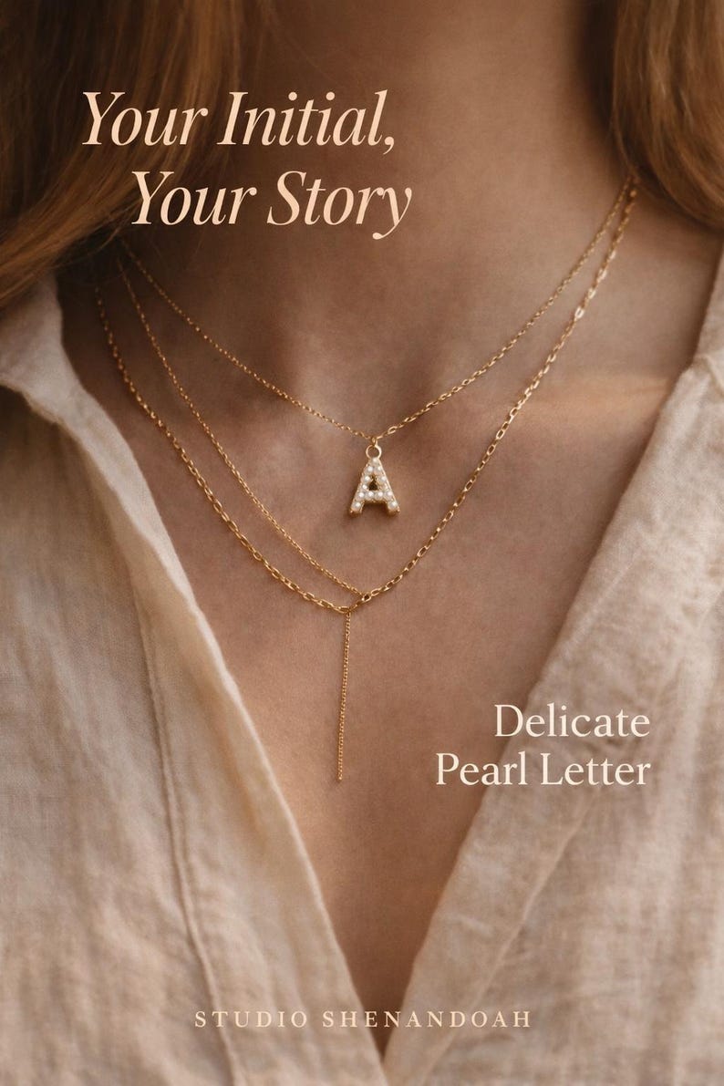 Pu&ograve; includere: Collana a strati color oro con un ciondolo a forma di lettera "A" tempestato di perle. L'immagine include il testo "Your Initial, Your Story" e "Delicate Pearl Letter". Il logo Studio Shenandoah &egrave; in basso.