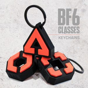 May include: Three black and orange keychains with a geometric design. One keychain is triangular, and the others are hexagonal. The keychains have a black ring attached. The text "BF6 CLASSES KEYCHAINS" is in the background.