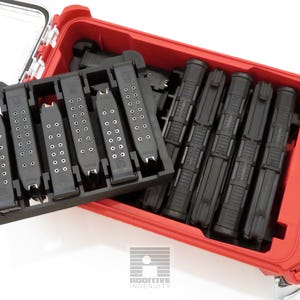 May include: A red storage case with a clear lid, containing black magazine holders and magazines. The case is open, revealing the contents. The magazines are arranged in a black holder and inside the case.