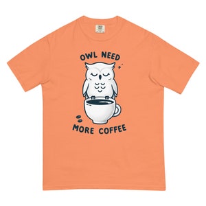 Peut inclure: Un t-shirt couleur pêche avec un hibou blanc tenant une tasse de café. Le texte "OWL NEED MORE COFFEE" est imprimé sur le t-shirt.