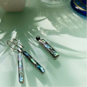 May include: A set of iridescent abalone shell earrings and a pendant necklace. The jewelry pieces are silver-toned and feature a rectangular shape with a multi-colored abalone shell inlay.