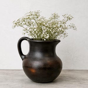 Puede incluir: Una taza de cerámica blanca con un asa negra y el texto "But First, Coffee" en negro, con una fuente de estilo manuscrito. La taza está sobre una superficie blanca.