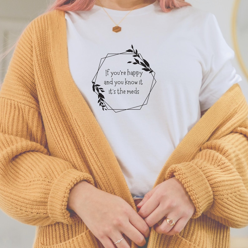 May include: White t-shirt with a black graphic design featuring a geometric frame with leaves and the text "If you're happy and you know it it's the meds".
