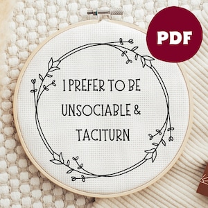 Puede incluir: Un aro de bordado blanco con una corona floral negra y el texto "Prefiero ser insociable y taciturno".