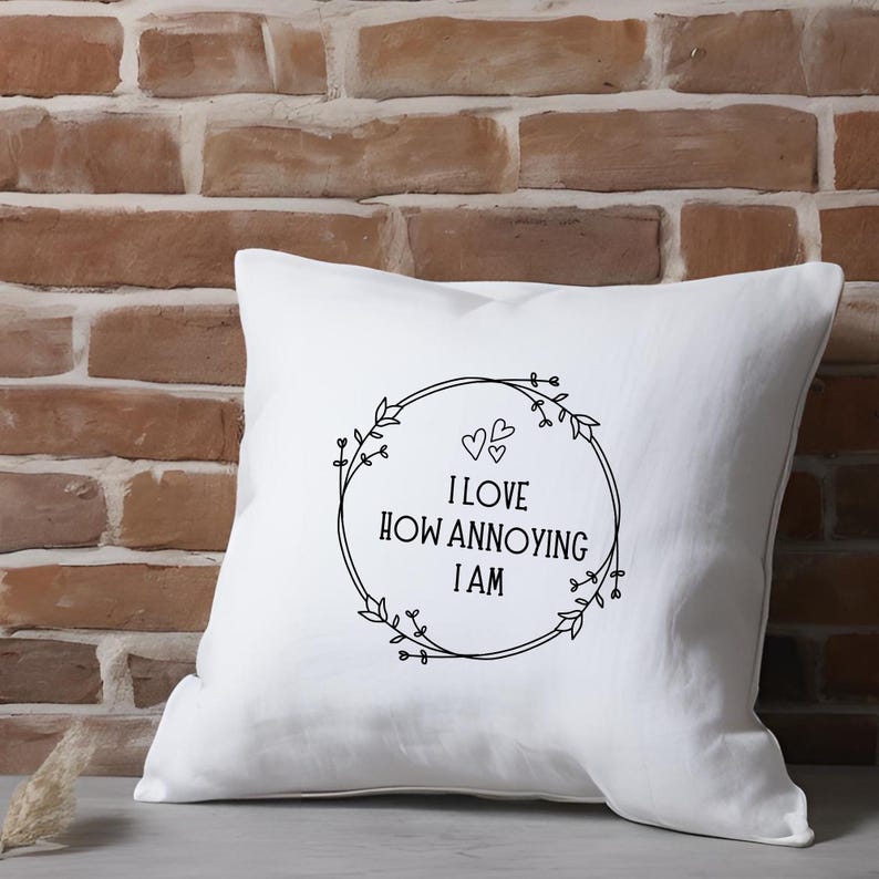May include: White throw pillow with black text and a floral wreath design. The text reads "I love how annoying I am".